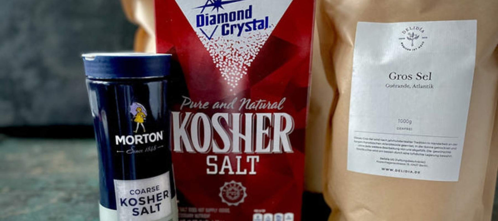 Auf einem Tisch stehen Packungen von Morton coarse salt, Diamond Crystal Kosher Salt, Delidía grobes Meersalz