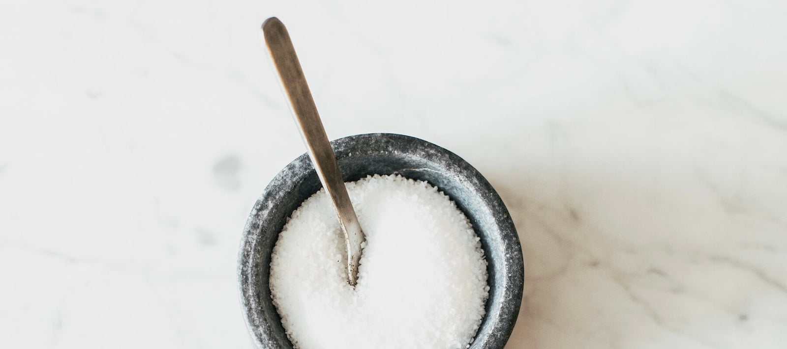 Jodsalz in einem runden Gefaess mit einem Löffel auf einem Marmortisch